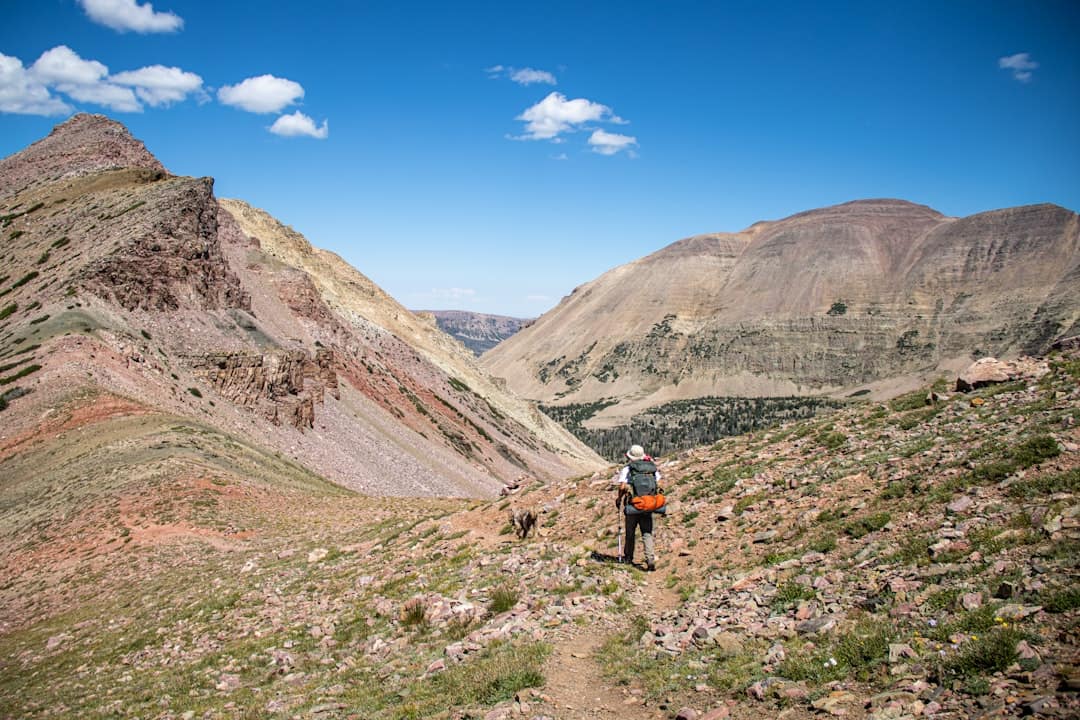 Hiker with backpack on mountain trail under blue sky.